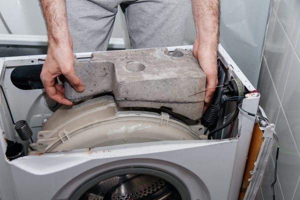Handyman repairing a washing machine. The hands of a man disassemble the washing machine. Repair and dismantling of the washing machine. Close-up