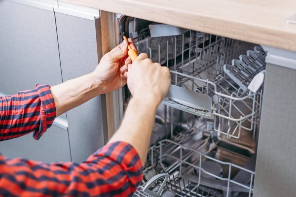 man repairing dishwasher. Male hand with screwdriver installs kitchen appliances, close up