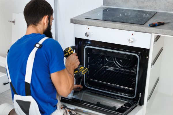 Man installs the oven after assembling the kitchen and screws the bolts with a screwdriver