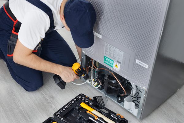 Male technician repairs a refrigerator in the kitchen in close-up